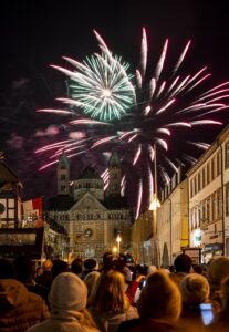 Kleine grüne und große rote Feuerwerksblume über dem Dom, beibachtet von zahlreichen Menschen auf der Maximilianstraße