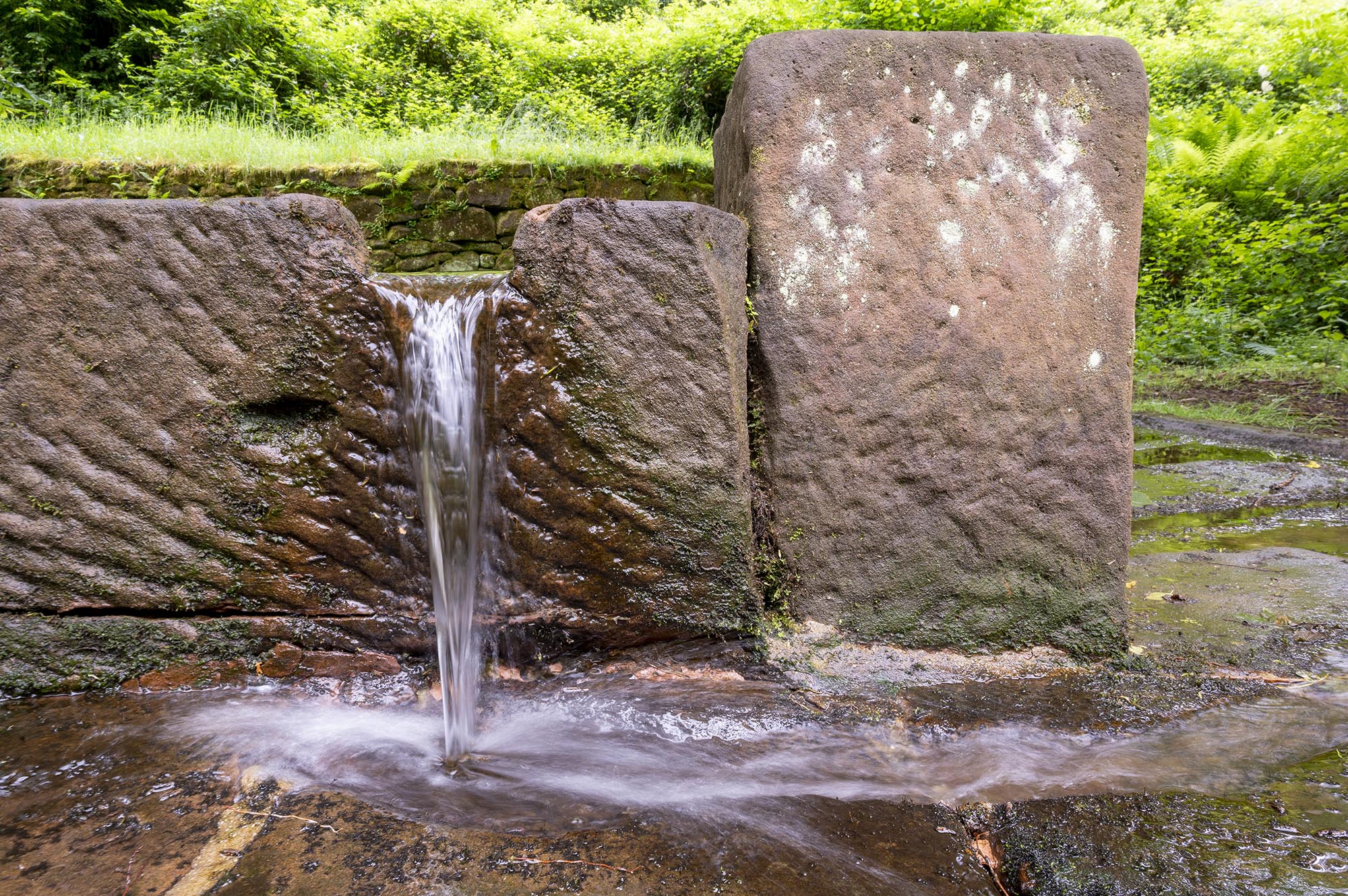 Nahaufnahme Straufelsbrunnen, aus dem Wasser aus rechteckig behauenen braunen Steinen läuft.
